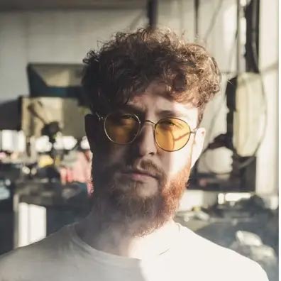 Barber 1 young man with beard smiling and wearing a brown shirt